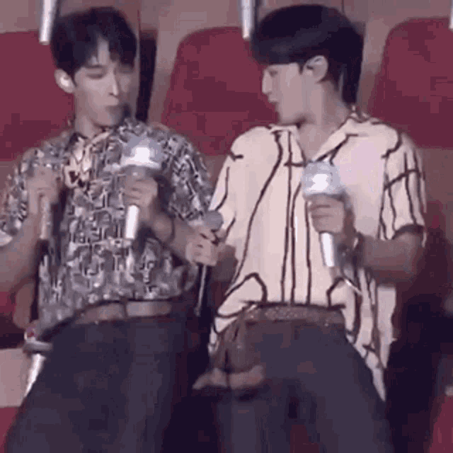 two young men are sitting next to each other in a theatre holding microphones .