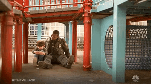 a man sits on the ground with a child in a playground with #the village
