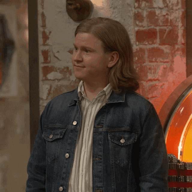 a man wearing a denim jacket and striped shirt stands in front of a jukebox