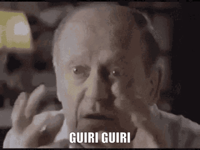 an older man is making a funny face with his hands and the words guiri guiri written on his face .