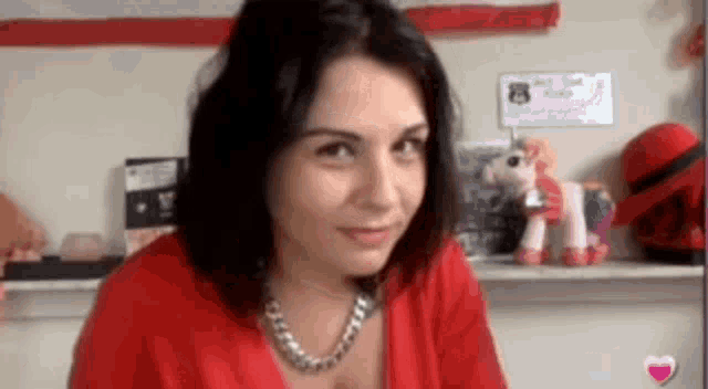 a woman in a red shirt is sitting in front of a shelf with stuffed animals on it