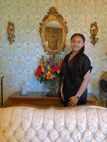 a woman in a black dress stands in front of a mirror and a vase of flowers