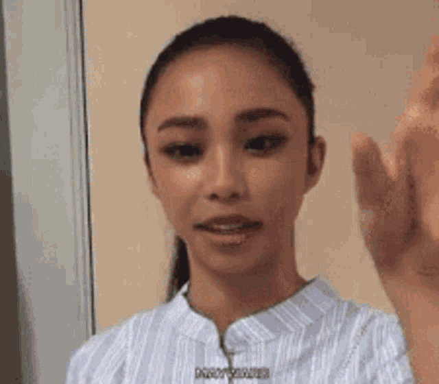 a woman in a blue and white striped shirt is waving her hand .