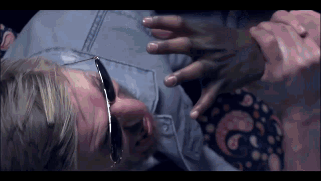 a man wearing sunglasses holds another man 's hand while laying on the floor