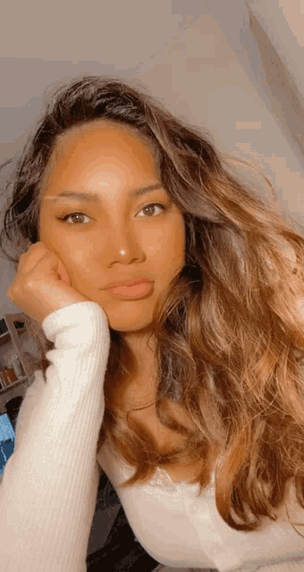 a woman wearing a white sweater has her hand on her face