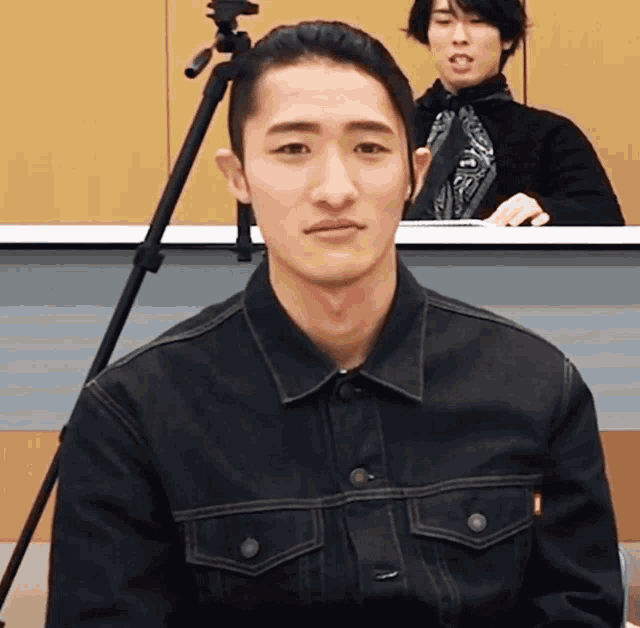 a man in a black denim jacket is sitting in front of a camera