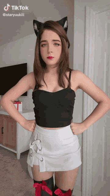 a woman wearing a cat ear headband and a white skirt is standing with her hands on her hips