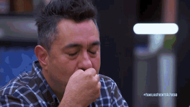 a man in a plaid shirt is crying with the hashtag familiasfrentealfuego on the bottom right
