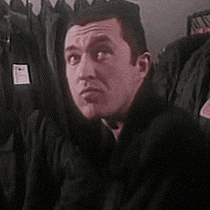 a man in a black jacket is making a funny face while sitting in front of a row of jackets .