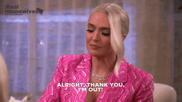 a woman in a pink suit is sitting at a table and saying alright thank you i 'm out .