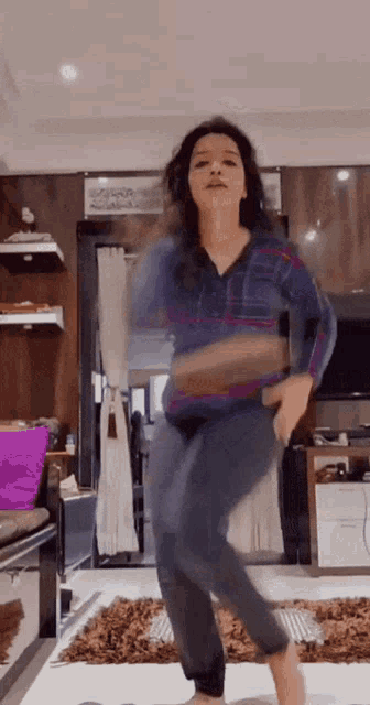 a woman in a blue shirt and jeans is dancing in a living room .