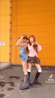 two women are standing next to each other in front of a yellow building .