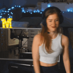 a woman wearing headphones and a white tank top stands in front of a yellow letter m