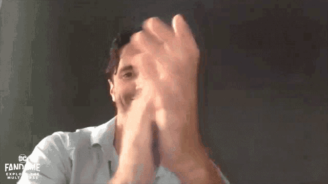 a man clapping his hands in front of a screen that says dc fandome explore the multiverse