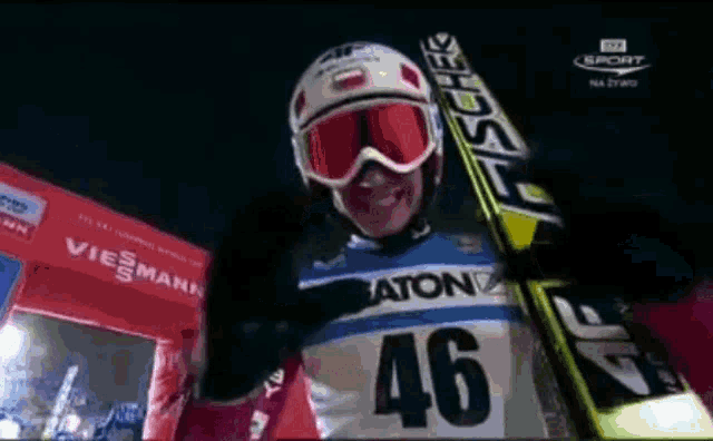a man wearing a helmet and goggles holds a pair of skis with the number 46 on it