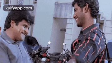 two men are standing next to each other in front of motorcycles and smiling at each other .