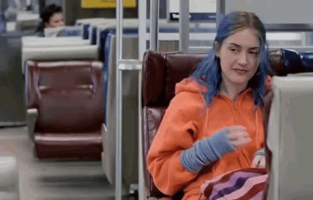 a woman with blue hair is sitting on a bus looking at a computer screen .