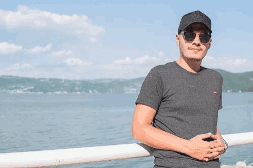 a man wearing sunglasses and a hat is leaning against a railing near the water