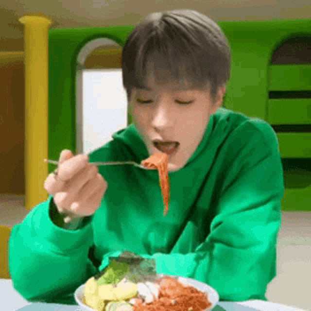a young man in a green sweatshirt is eating spaghetti with a fork .