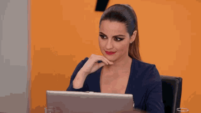 a woman is sitting at a desk with a laptop and making a funny face .