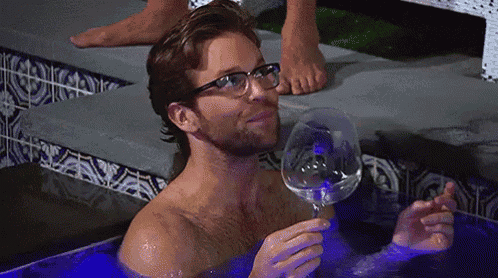 a shirtless man is taking a bath and holding a wine glass .
