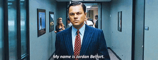 a man in a suit and tie is standing in a hallway and saying my name is jordan belfort .