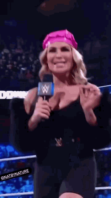 a woman is wearing a pink hat and holding a microphone while standing in a wrestling ring .