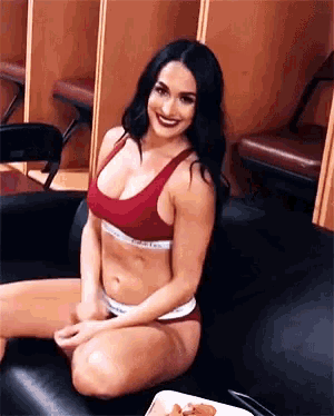 a woman in a bikini is sitting on a couch in a locker room smiling .