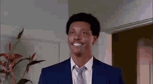 a man in a suit and tie is smiling while standing in front of a plant .