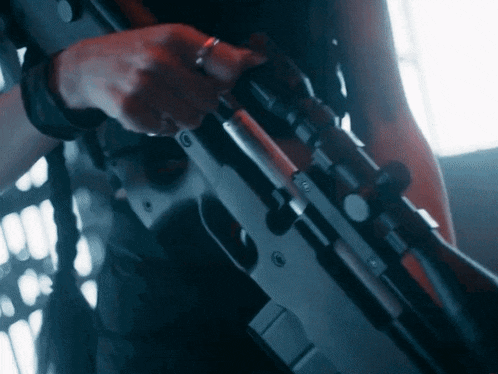 a close up of a person holding a sniper rifle with a ring on their finger