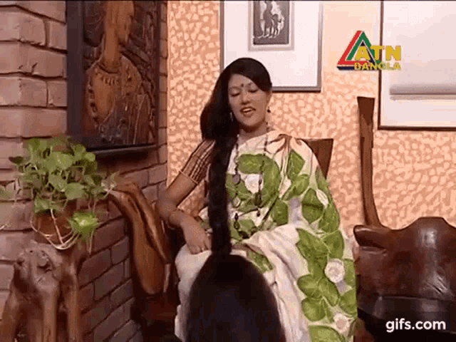 a woman in a green and white saree is sitting in a chair with her hair very long .