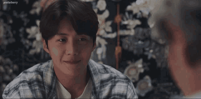 a man in a plaid shirt is looking at another man in front of a floral wallpaper