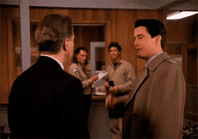 a man in a trench coat is talking to two other men