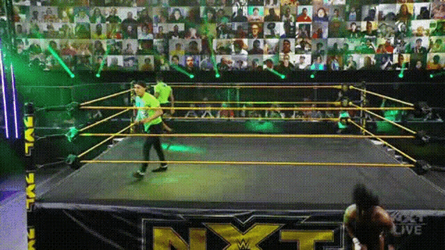 a man in a green shirt is standing in a wrestling ring with a crowd watching .