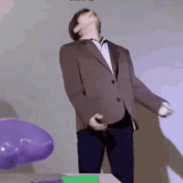 a man in a suit and tie is standing in front of purple balloons .