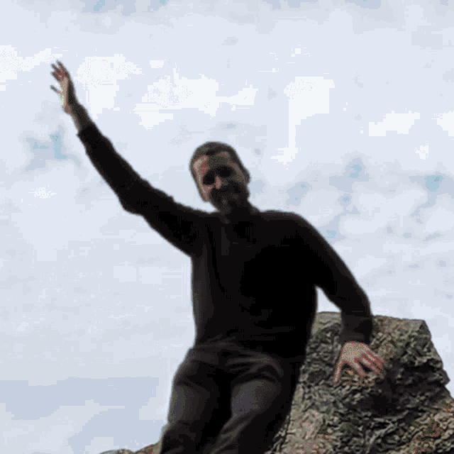 a blurry picture of a man standing on a rock with his hand up in the air .