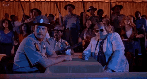two police officers sitting at a table in front of a crowd with giant monster written on the screen