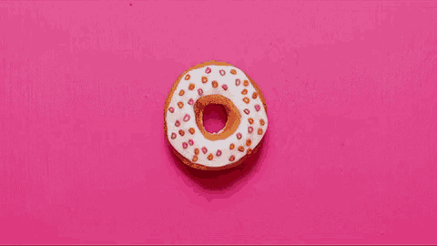 a man and a woman are reaching for a doughnut on a pink surface