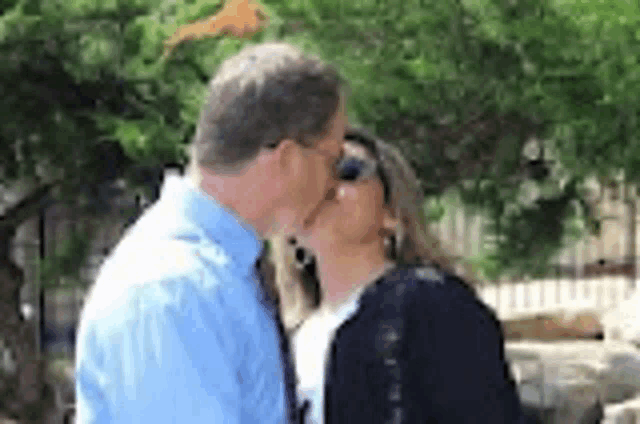 a man and woman are kissing in front of trees .