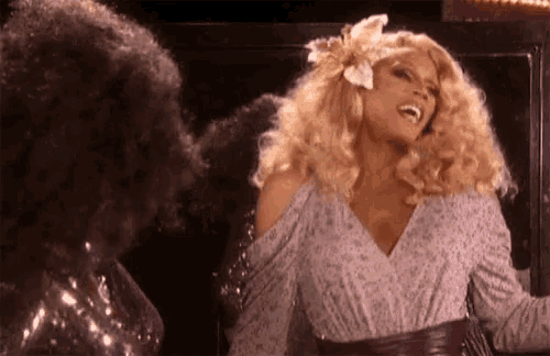 a woman with blonde hair and a flower in her hair is standing next to a woman with afro hair .