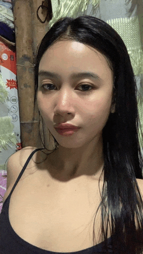 a woman in a black tank top looks at the camera in front of a bamboo pole