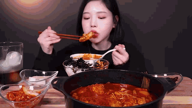 a woman is eating a bowl of food with chopsticks and a pot of food