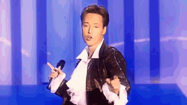 a man is singing into a microphone while wearing a black jacket and white ruffled shirt .