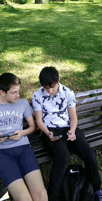 two boys are sitting on a park bench and one of them is wearing a shirt that says original jacks