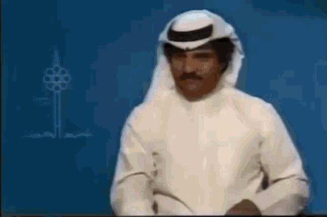 a man with a mustache is wearing a white robe and a white head scarf .