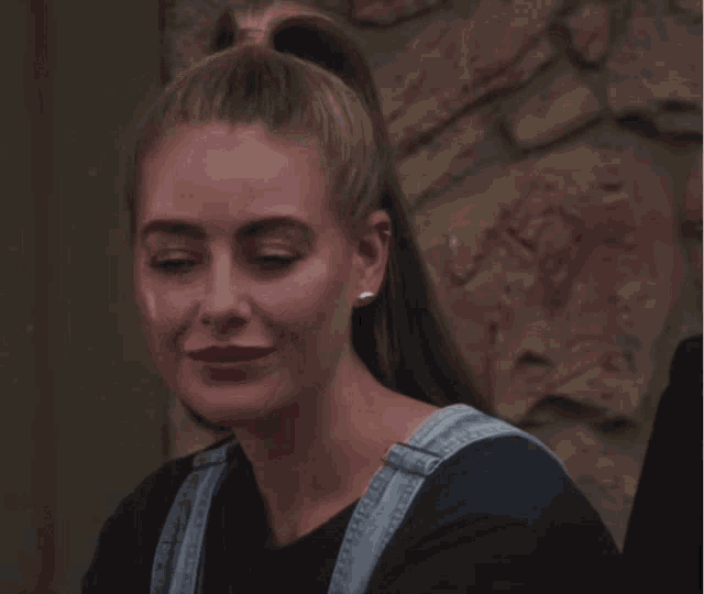 a woman with a ponytail and overalls looks sad