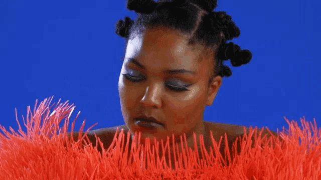 a woman with dreadlocks is standing in front of a blue background and looking down