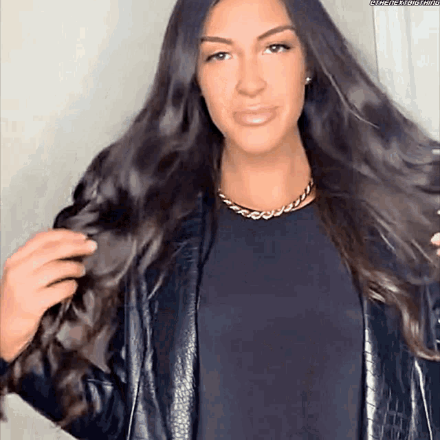 a woman with long dark hair is wearing a black jacket and a gold chain necklace .