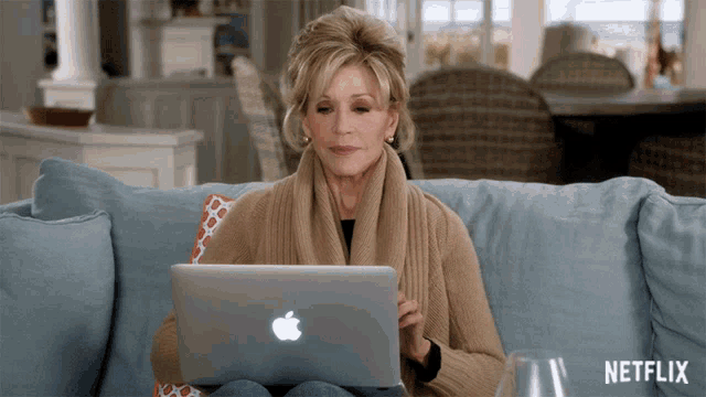 a woman sits on a couch using an apple laptop with netflix written on the bottom