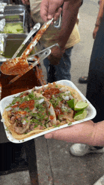 a person is holding a styrofoam tray of tacos with a spoon in it